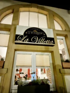 Beleuchtetes Schild und einladende Außenansicht des italienischen Restaurants La Villetta in Durlach bei Nacht.